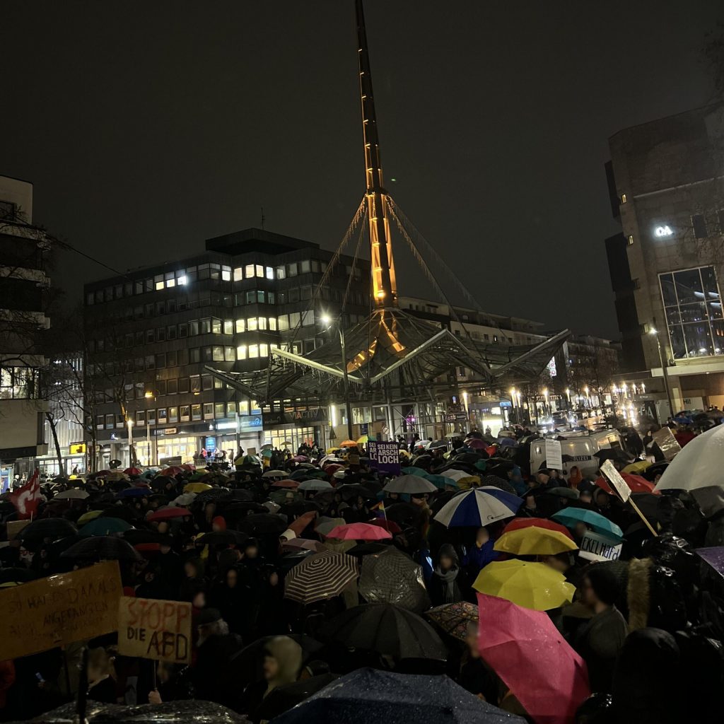 Mehrere tausend Menschen stehen bei Regenwetter auf dem Platz hinter der Reinoldikirche in Dortmund, es sind viele Regenschirme und Schilder mit Parolen gegen die AfD zu sehen.